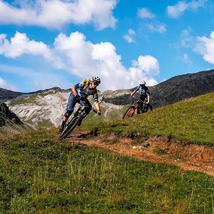 Two mountain bikers riding down a trail in the mountains.